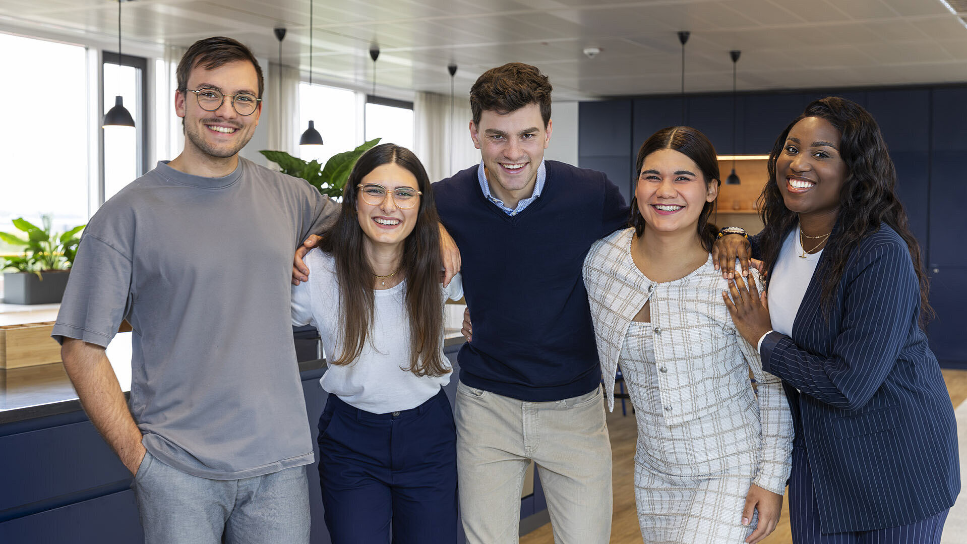 Fünf Azubis stehen Arm in Arm und lächeln in die Kamera