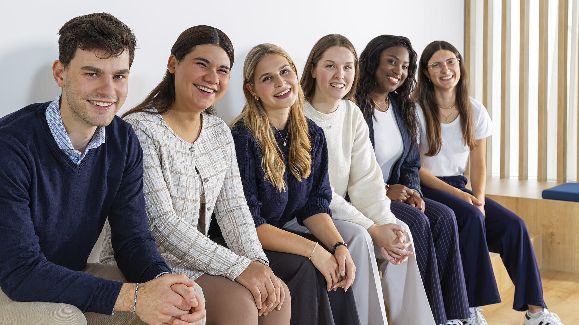 Mehrere junge Leute sitzen nebeneinander auf einer Bank und lächeln in die Kamera